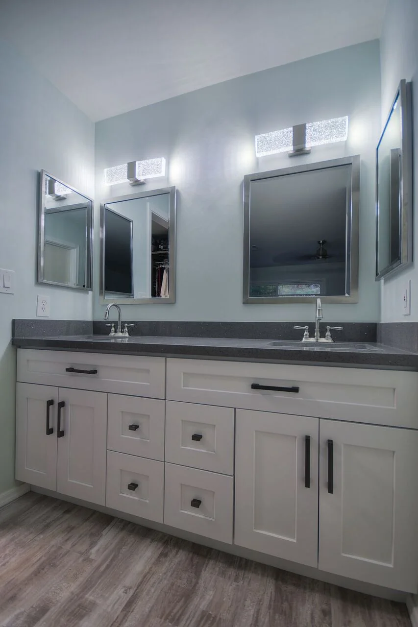 Dual-sink bathroom vanity with white cabinetry, gray quartz countertop, and LED-lit mirrors