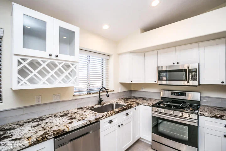 White kitchen cabinets, granite countertops, stainless steel appliances, and recessed lighting