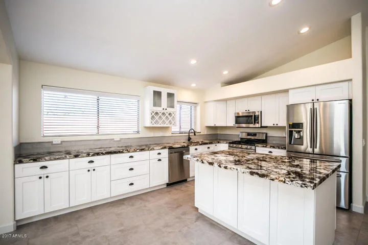 White kitchen cabinets with black granite countertops, stainless steel appliances, and island