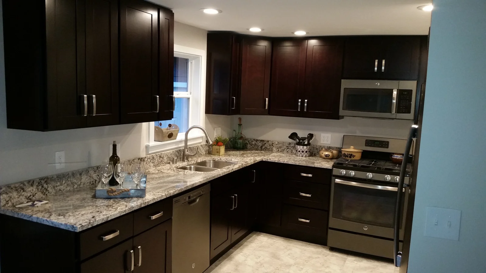 Dark wood cabinetry, granite countertops, stainless steel appliances, and recessed lighting in modern kitchen