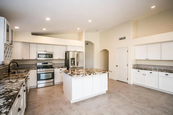 White kitchen cabinets, granite countertops, stainless steel appliances, center island with waterfall edge