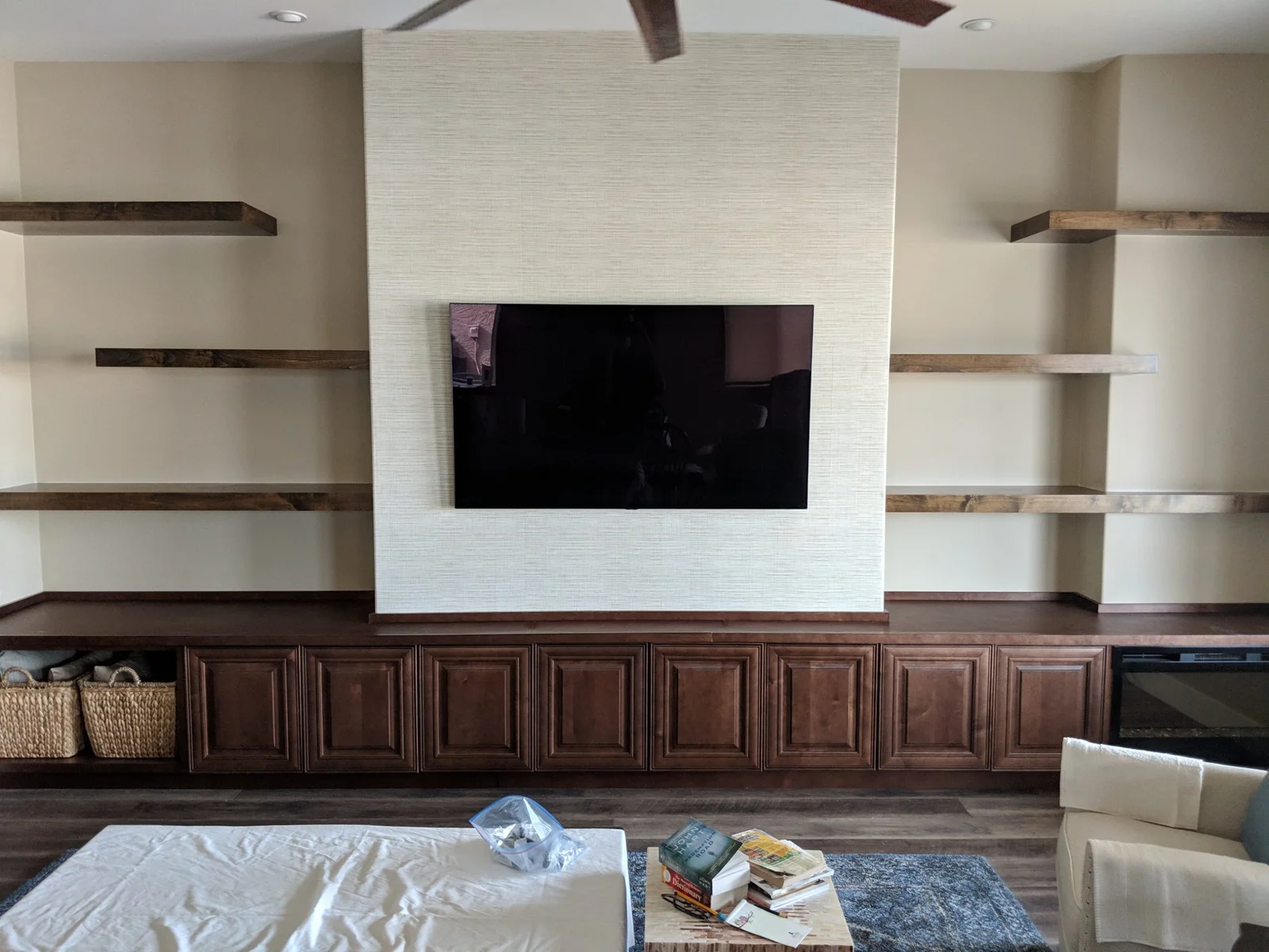 White brick accent wall with mounted TV, dark wood cabinetry, and floating wood shelves