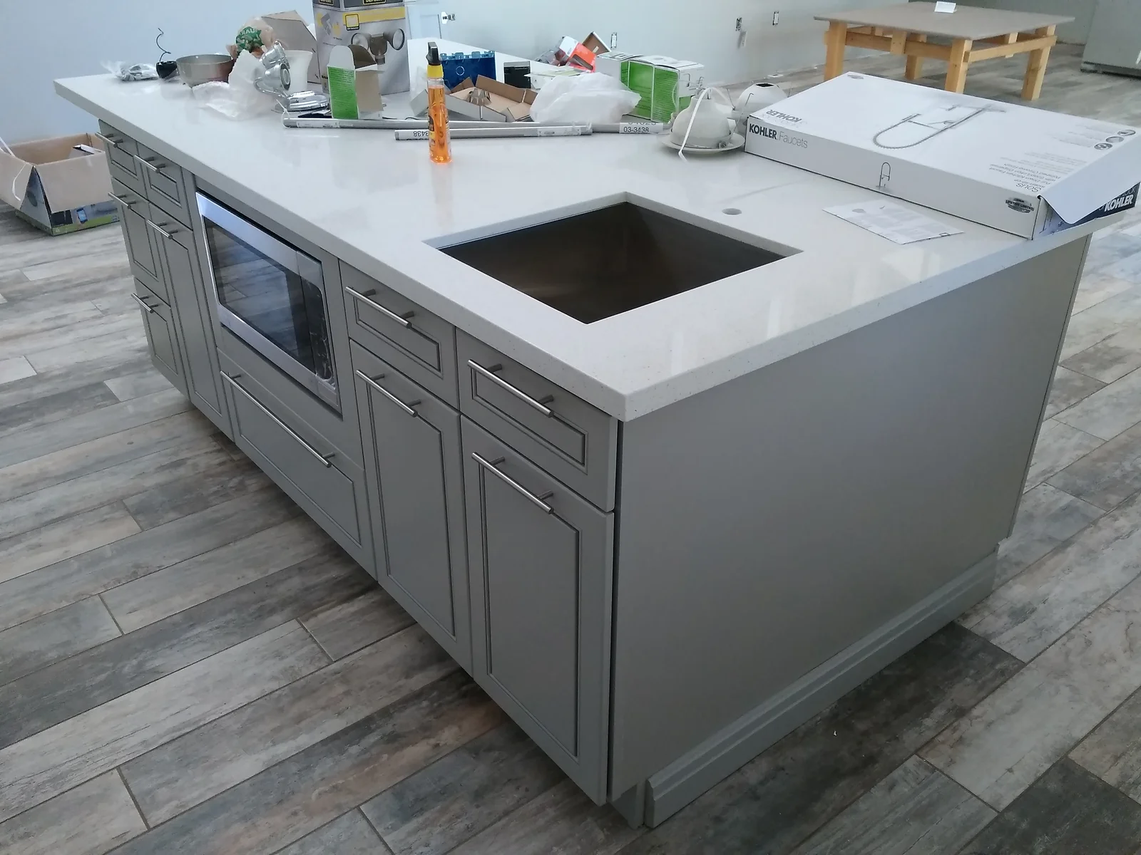 Gray kitchen island with white quartz countertop, stainless steel appliance, and luxury vinyl plank flooring