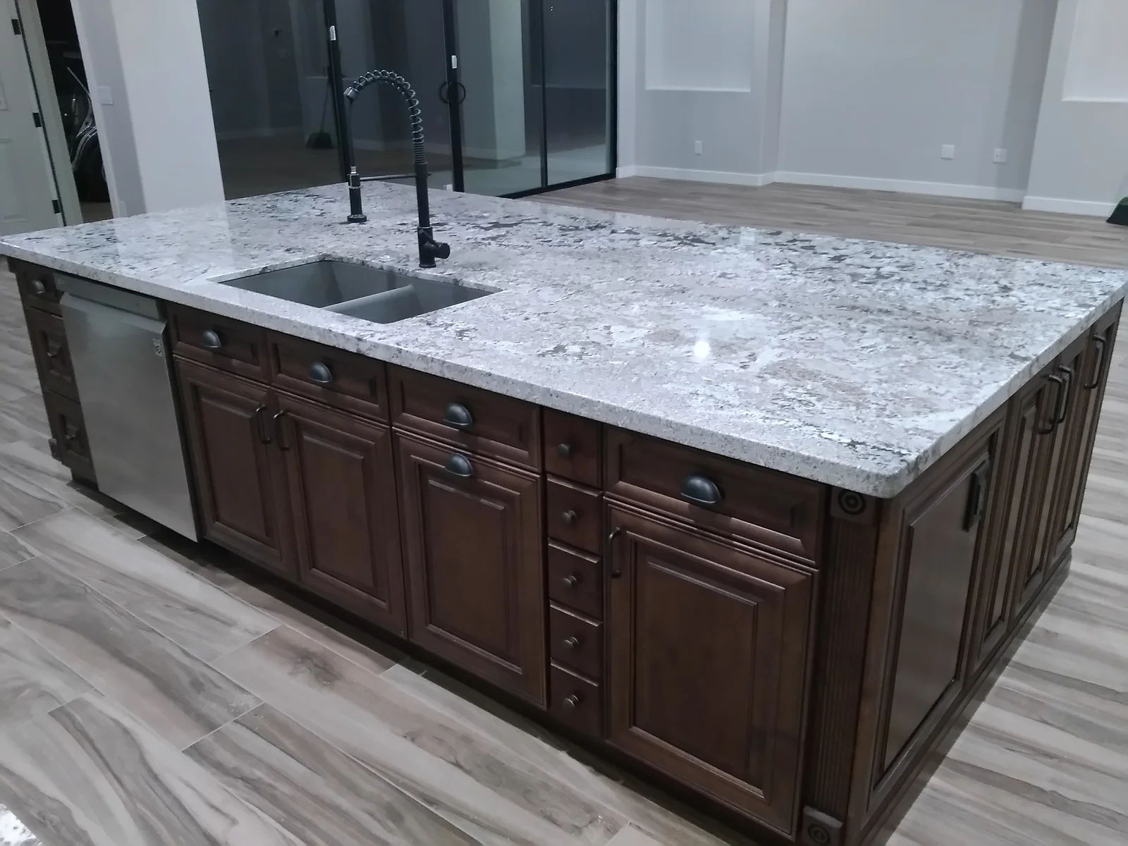 Light gray granite island countertop with undermount sink, dark wood cabinetry, and stainless steel appliances