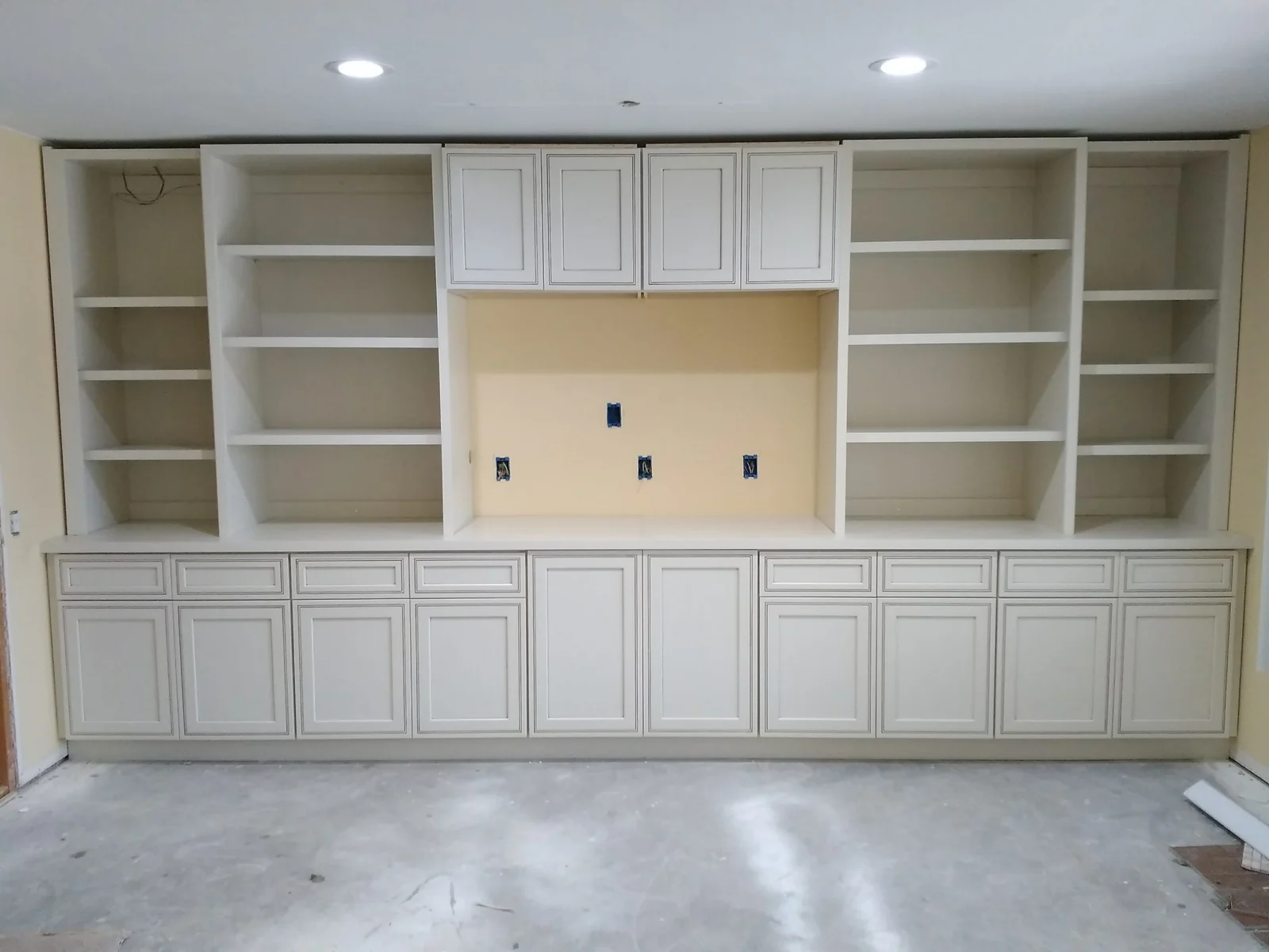 White painted built-in cabinetry with open shelves, glass-front upper cabinets, and lower drawer storage with media niche