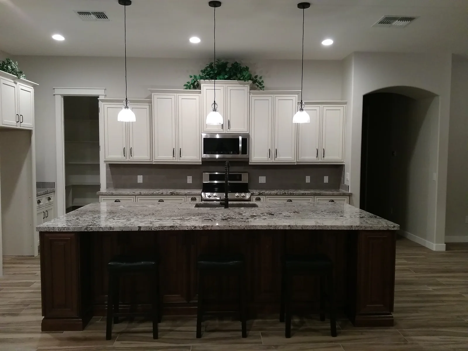 Modern kitchen with white cabinets, dark island, granite counters, and pendant lighting