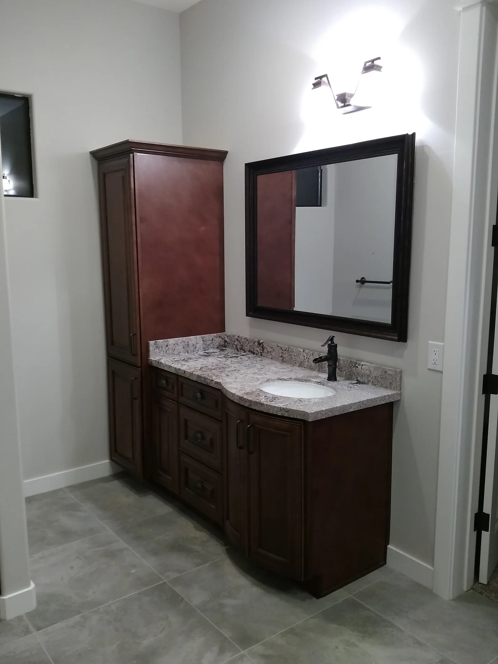 Dark wood bathroom vanity with granite countertop, undermount sink, and black-framed mirror